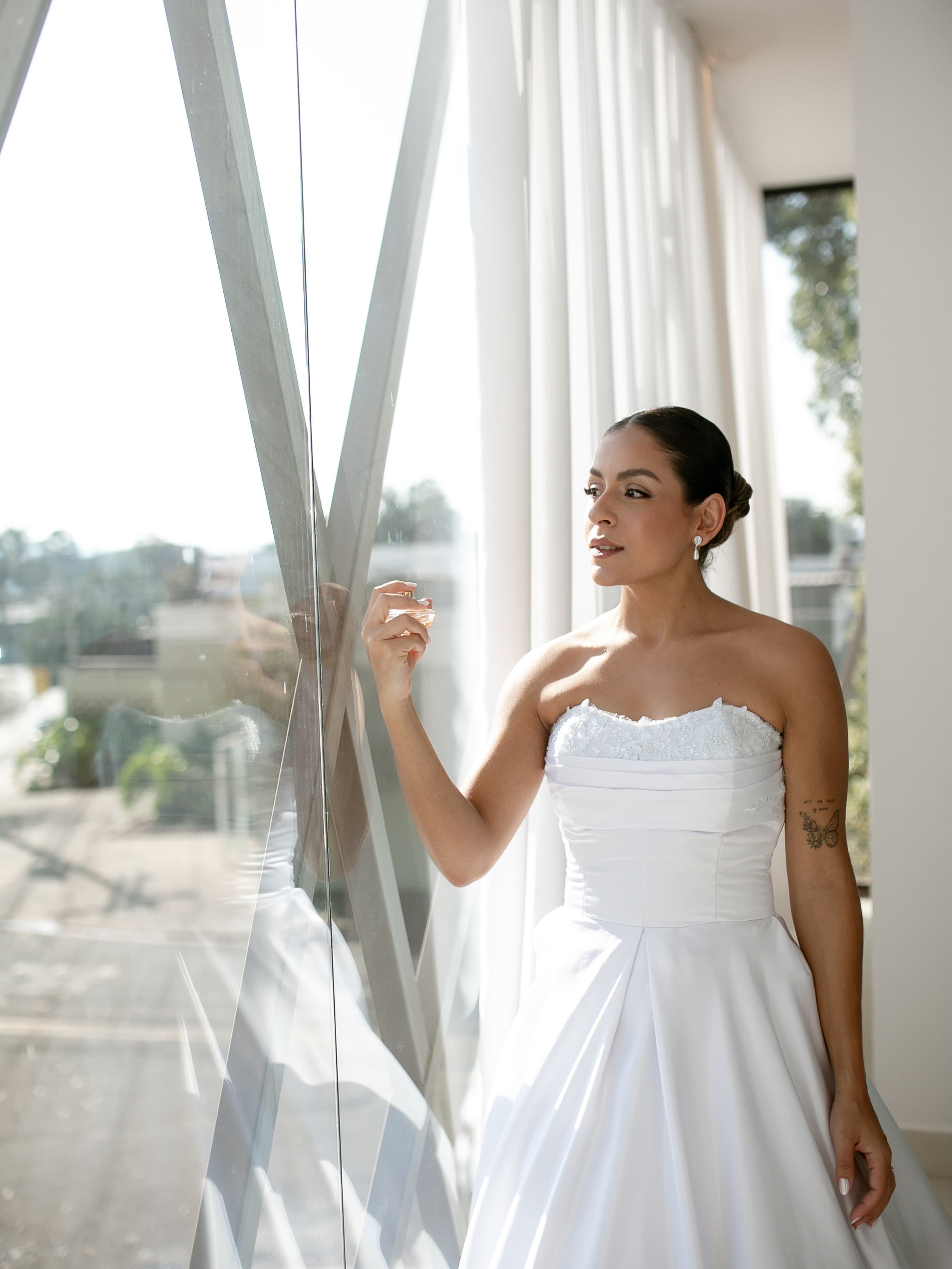 A mesma noiva sentada na poltrona dourada do salão, de robe branco, com o espelho ao fundo